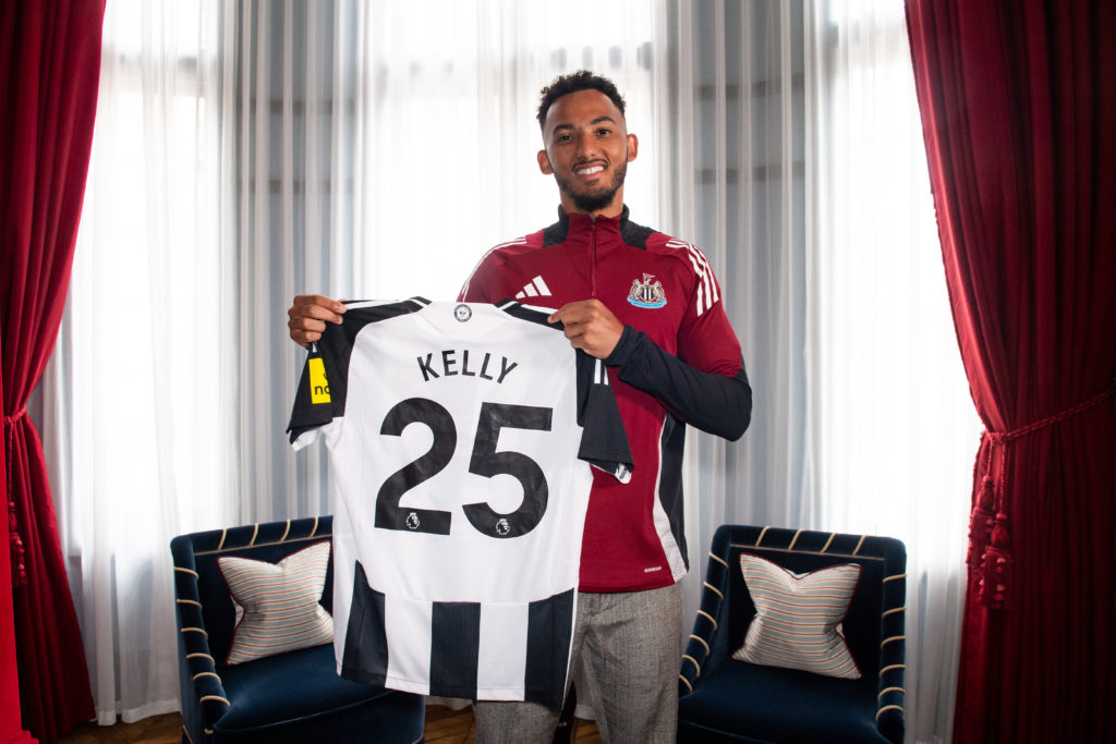Lloyd Kelly Signs For Newcastle United and holds a shirt with his name on the back.