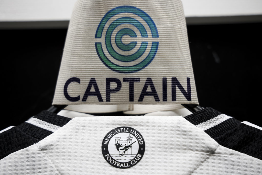 The back of a Newcastle United football shirt featuring an old badge and a captain's armband.