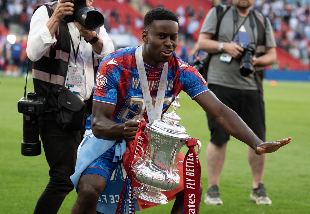 Marc Guehi prepares to lift the FA Cup trophy in the air in front of Crystal Palace fans after beating Manchester City at Wembley.