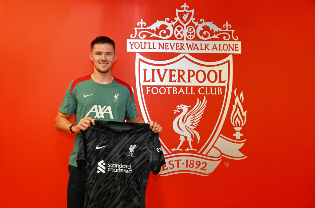 Freddie Woodman poses with the Liverpool shirt in front of the Liverpool crest.