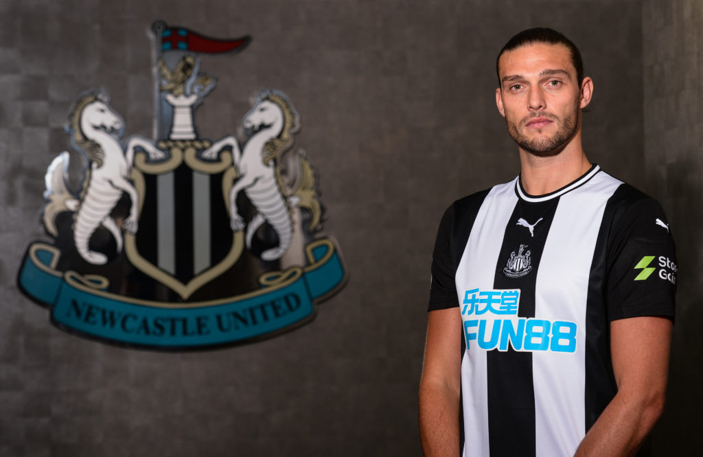 Andy Carroll posses in front of a Newcastle United badge after signing.