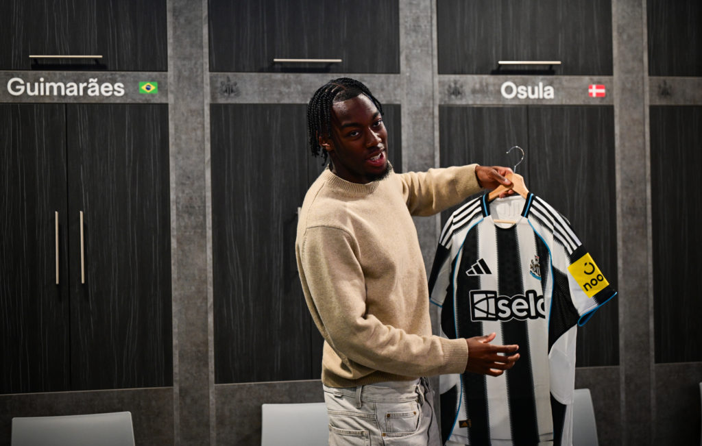 Anthony Elanga holds a Newcastle United home shirt inside the club's training ground dressing room.
