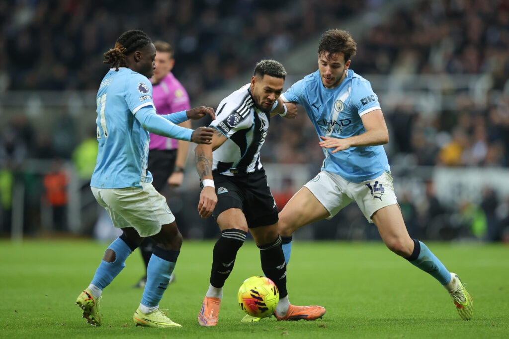 Joelinton battles for possession with Nico Gonzales and Jeremy Doku during Newcastle United's Premier League match against Manchester City.